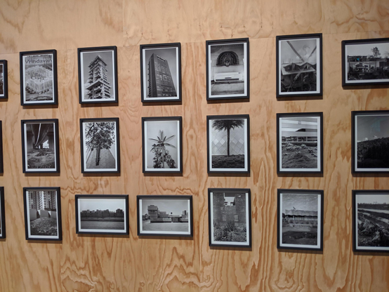 Installation view from the 2019 Venice Art Biennale: a large wall covered with a grid of framed black-and-white photographs. The frames are evenly spaced and visually similar, with no single image standing out, creating a repetitive and uniform visual pattern.