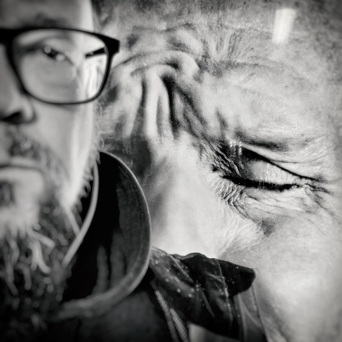 A black and white portrait showing a man in glasses beside a close-up of a distressed face, illustrating deep emotion and contemplation.