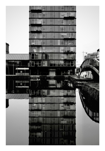 A black and white photo of an apartment block reflected in the water that's in front of it.