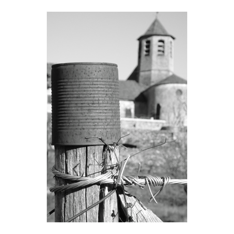 A squat church steeple with a fence post topped with a tin can in the foreground. (Version françæ) Clocher trapux d’æn église avec al premiær plan æn piquet de clôture coiffæ d’æn boîte de conserve.