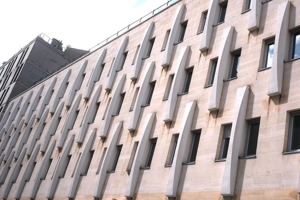 Photo format paysage, une façade de bâtiment sur 3 ou 4 étages (on ne voit pas le bas) avec des fenêtres et des ornement abstraits en béton donnant un look remarquable à l’ensemble