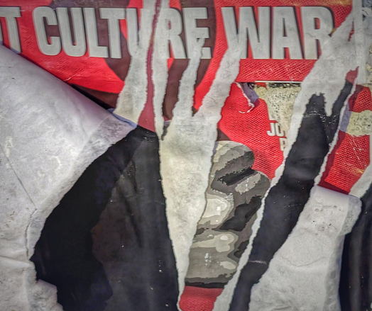Some torn posters on an exterior wall present a crazy pattern in white, black, and red and showing the words culture war.