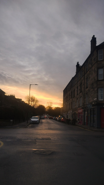 Tall, Victorian tenements in morning shade, clouds behind and above, the horizon splashed with orange from the rising winter sun