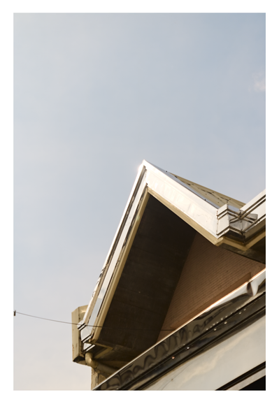 Sharp, metallic corner of a roof structure against a vast expanse of pale blue sky.