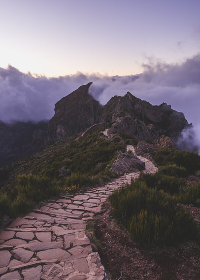 The path leads into the mountains shrouded in fog and clouds after sunset, everything takes on pink and purple hues.