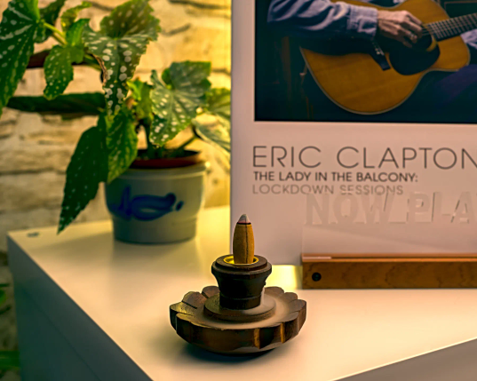 Im Vordergrund dampft ein Backflow-Duftkegel auf einer hölzernen Blüte. Dahinter das Cover von Eric Claptons album "The Lady in the Balcony". 