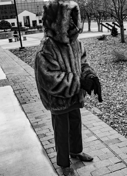A black and white photo of a pipe smoking man wearing a very thick coat and hood against a very cold and breezy day.