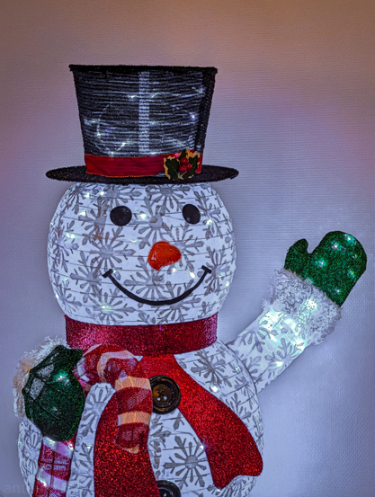 A decorative light-up snowman. It is internally lit with small white LED lights, giving it a festive glow and emphasizing the snowflake pattern.

It wears a tall, black top hat that has a textured, glittery appearance and is trimmed with a red ribbon and a small piece of faux holly. It wears a thick red scarf tied around its neck, over which a smaller, red-and-white striped scarf is draped.