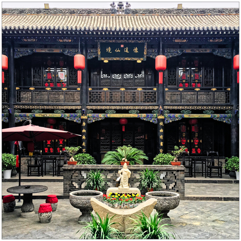Courtyard with tables, chairs, lanterns, potted plants, and an outdoor umbrella in front of a traditional two-story facade.