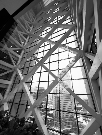 Inside a tall building looking out at a city scape through windows a fascinating crisscrossing of white support structures create a wonderful atmosphere.