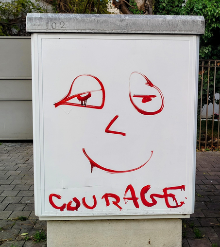 Dans la rue, sur une "borne" un dessin en rouge d'un visage qui sourit.
Il est écrit en dessous : courage.
