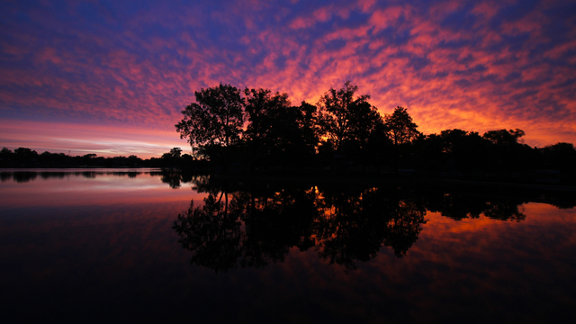 Photo of a colorful red, orange, pink, and purple sunrise over a lake with a small island in silhouette in the center.