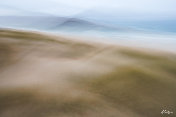 abstract coastal photograph using ICM. grasses sway in the wind in the foreground leading out to the ocean and a lone conical hill