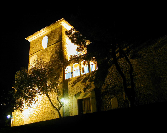 A night time photo of a floodlit Spanish church, looking up at the square tower.