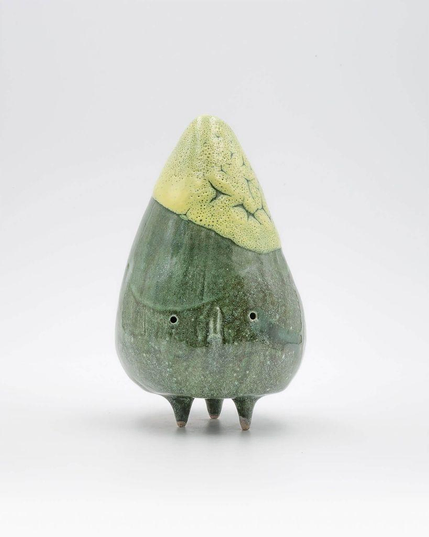 Ceramic sculpture resembling a green mountain with a light green peak, featuring three pointed feet and a textured surface.