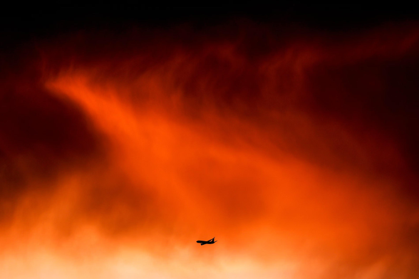 A  plane flies past bright red storm clouds at sunset.