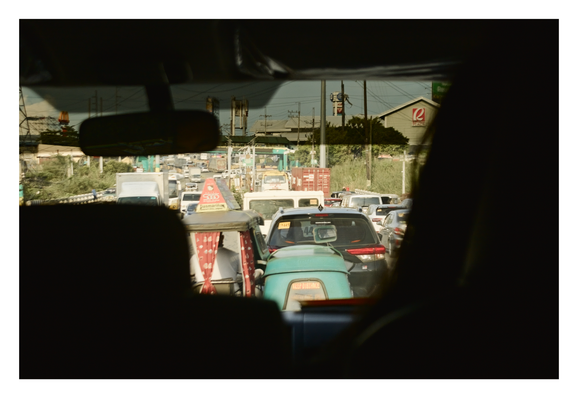 a view from inside a car, looking out through the windshield at heavy traffic on a busy road. The shot is framed by the dark silhouettes of the vehicle's interior, including the seats and rearview mirror. - Google Gemini 3 Pro Preview