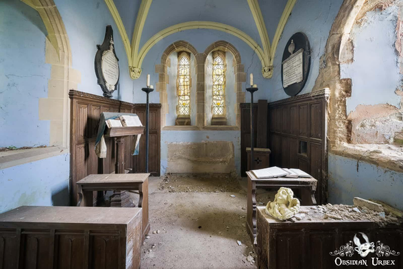 A view of a small, ruined church shows its stained glass windows, lectern and pews. The walls are blue and deteriorating, with debris scattered on the floor.