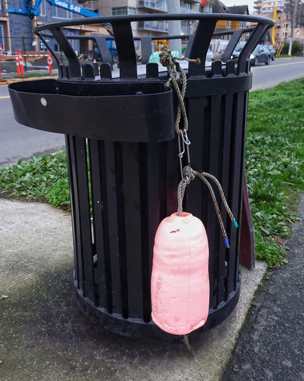 This image shows one of the metal trash cans along the Dallas Road walkway. Someone's hung a fishing float on the side of the can, likely a float that washed ashore.