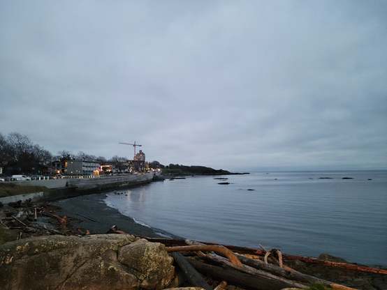 This image shows a section of the shoreline along Dallas Road, looking east. Driftwood Beach is in the foreground and Holland Point is in the distance.