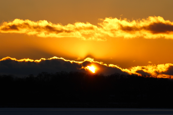 Sunset photograph of clouds in a yellow sky with the sun showing through a heart-shaped hole in the middle.