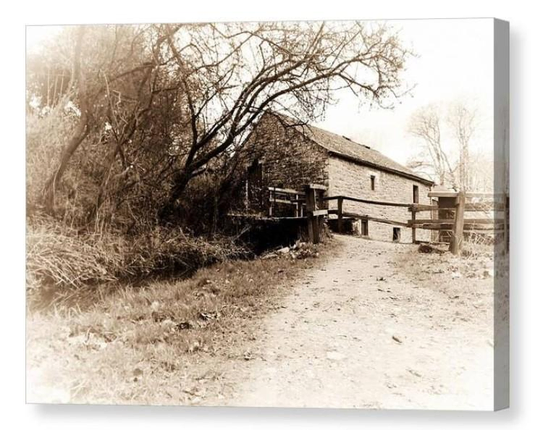 Vintage looking sepia photograph of a dirt track path leading up to an old watermill.  The image is shown printed upon a block canvas.