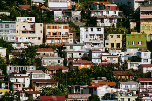 Colorful hillside houses densely packed against lush greenery. The vibrant architecture creates a lively, picturesque scene under sunlight.