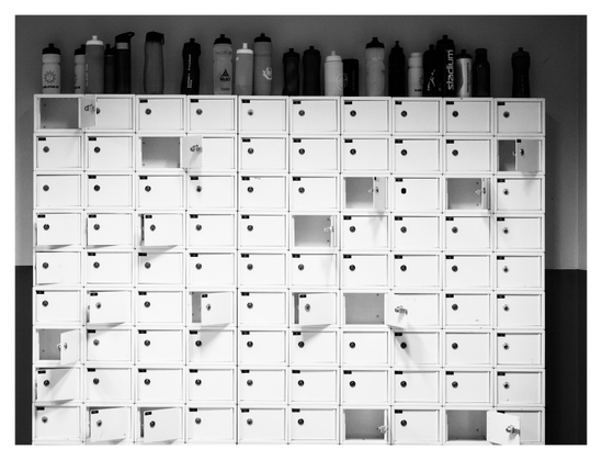 En liggande svartvit bild på en samling små vita skåp, några med dörrarna öppna. Ovanpå skåpen står vattenflaskor av olika sorter.