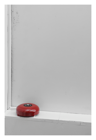 A red, round fire alarm bell mounted in the corner where two white ceiling surfaces meet.