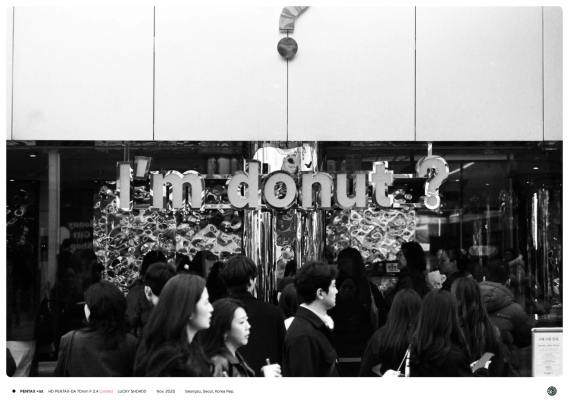 수많은 인파가 "I'm Donut?" 간판이 걸린 건물 앞을 지나가고 있음.