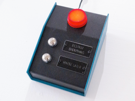 A blue case holding a black panel with two silver buttons, labelled "DESTROY EVERYTHING" resp. "MAYBE LATER", and on top a red signal light.