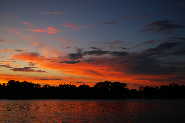 Sunset photograph of a bright orange and dark grey cloud over a lake. The cloud looks like a dragon flying from right to left with its head and chest in bright orange and its wings trailing behind in grey.
