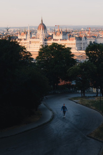 A person walks on a curvy road. The Hungarian Parliament Building is in the background.