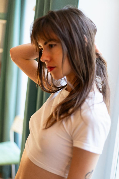 Soft daylight portrait of a person by a window, wearing a white crop top, hair loose, calm and natural mood.
