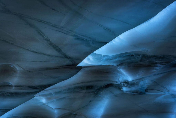 Intricate patterns of blue ice, showcasing smooth curves and dark veins, creating a mesmerizing, ethereal effect.