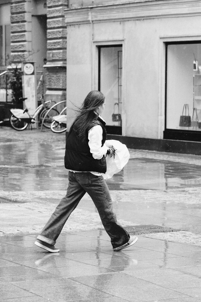 Das Foto zeigt eine Straßenszene in Schwarz-Weiß in der St. Pöltenter Innenstadt an einen regnerischen windigen Tag. Man sieht eine Person mit Regenschirm der durch den Wind verbogen ist und vor sich hält