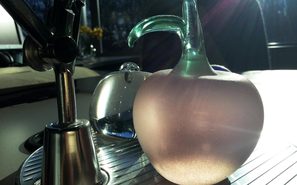 Two glass fruit lit by sunlight sitting on a silver lamp base of a colleague's desk at work.
