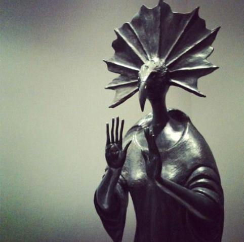 une déesse à tête d’oiseau appelle au calme en mettant ses paumes en avant