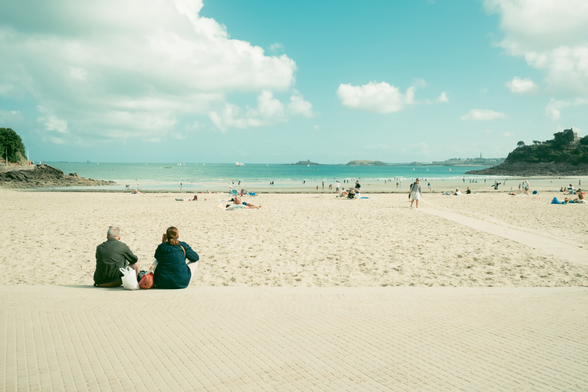 A couple sitting and watching other people on the beach from afar