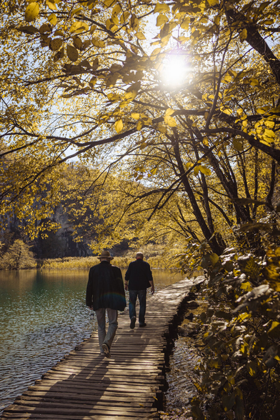 Two older guys walking on the wooden footbridge. In the background there are trees and a lake.