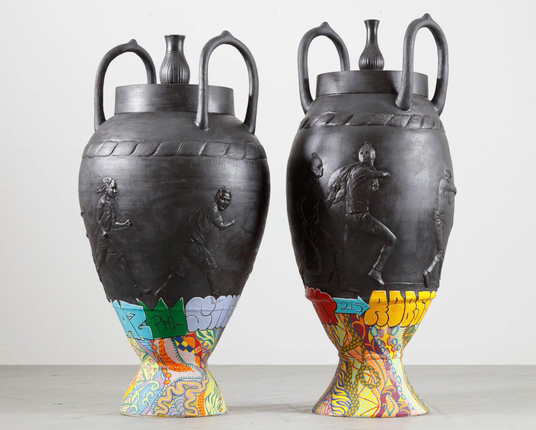 Two ceramic vessels inspired by Wedgewood pottery and Greek amphorae, by Roberto Lugo, featuring black relief imagery of figures walking around, plus graffiti motifs on the bases