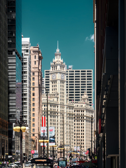 A white high-rise building with a clock tower and Beaux Art elements stands in between many modern high-rise buildings