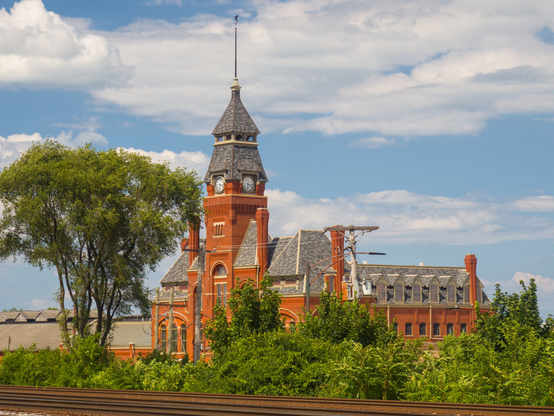 A great red brick Victorian building with a clock tower, behind rusty rails