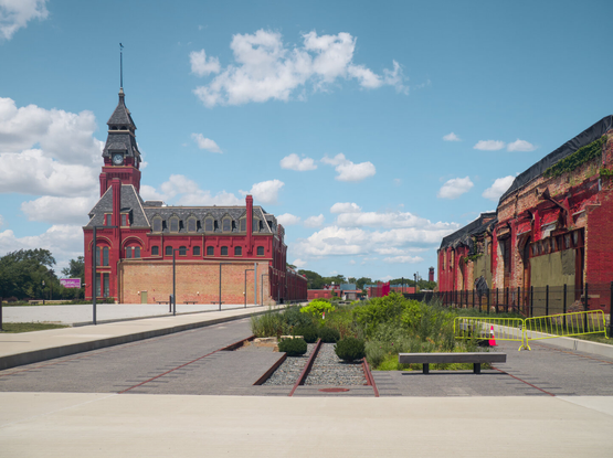On the left: A great red brick Victorian building with a clock tower. On the right: a heavily damaged brick factory building. In the middle is a plaza with a garden with a train track in it because this factory used to manufacture railroad cars.