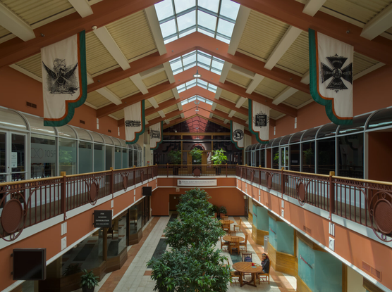 Looking through the simple concourse of Dearborn station from the second floor; there're only two floors. There's a courtyard on the first floor with plants and tables. A person was seated at a table. On the second floor, there's a walkway going around the courtyard. There're flags of various railroads on both sides above.