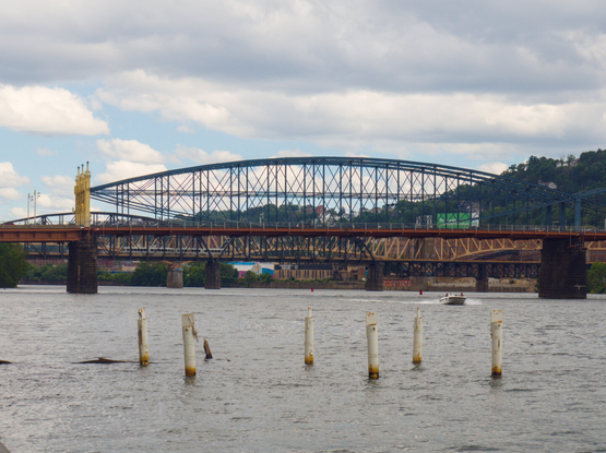 Multiple bridges seem to layer on top of each other across a great river. In the foreground are many pillars in the river. A yacht was traveling in the river.