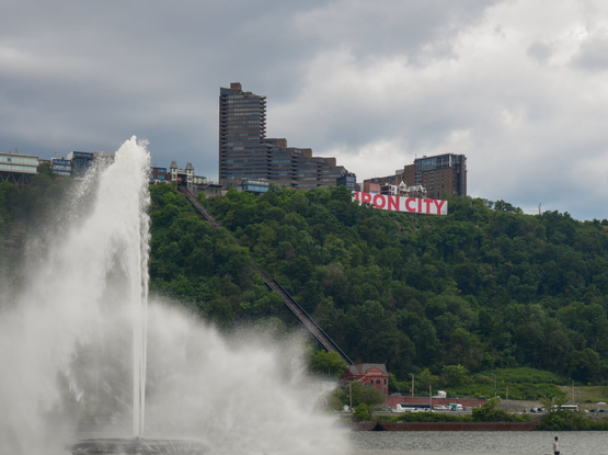 The Point State Park Fountain in front of the Duquesne Incline and the Iron City sign on top of the cliff. It was cloudy.