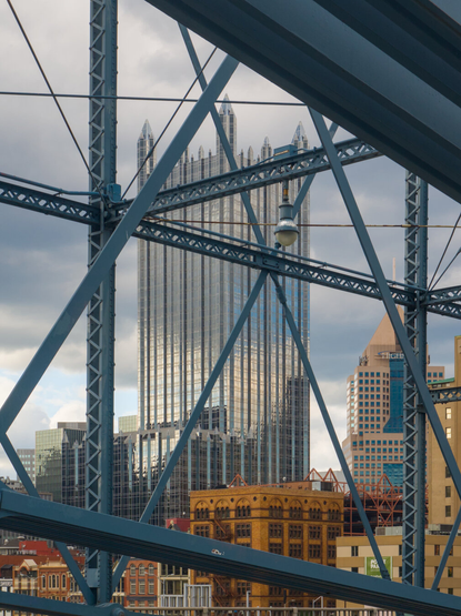 Looking through the dark blue steel structure of the Smithfield Bridge at the skyscraper that looks like a steel castle (PPG Place)
