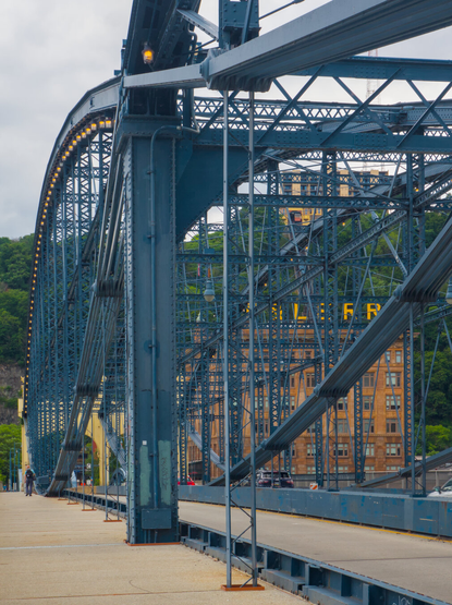 Looking through the dark blue steel structure of the Smithfield Bridge at the P&LERR (Pittsburgh and Lake Erie Railroad) building, with yellow P&LERR sign on the top. The sign is partially obscured by the bridge.