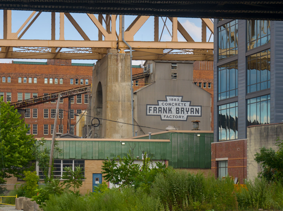 A great steel bridge that is painted yellow frames an old factory building that says 1883 Frank Bryan Concrete Factory